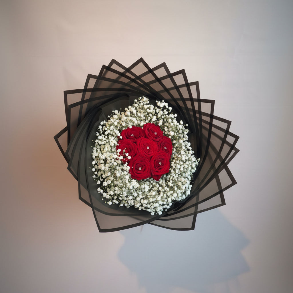 Decorative flower arrangement with red roses and white baby's breath in a black geometric container.