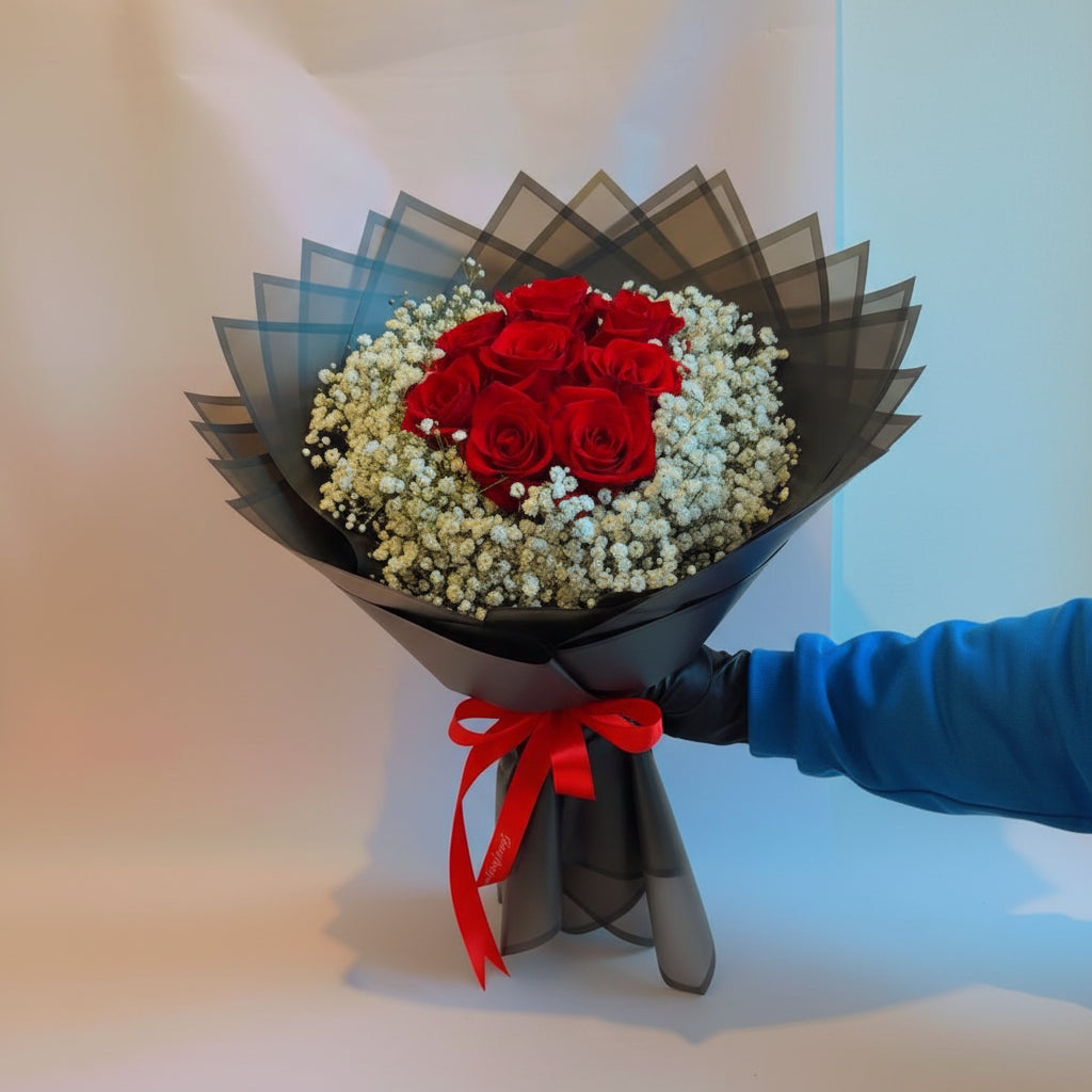 Bouquet of red roses with baby's breath wrapped in black paper, held by a gloved hand.