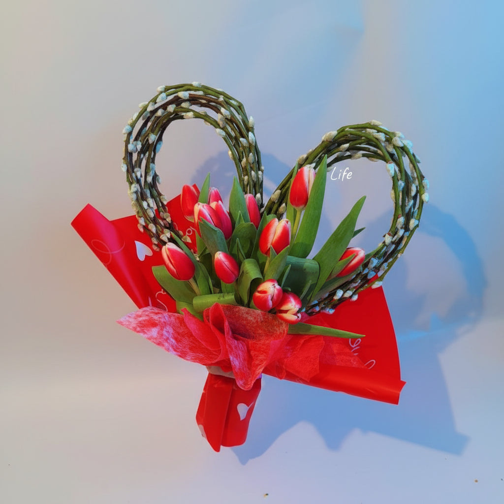 Bouquet of red tulips wrapped in red paper with a decorative heart-shaped bow on a light blue background.