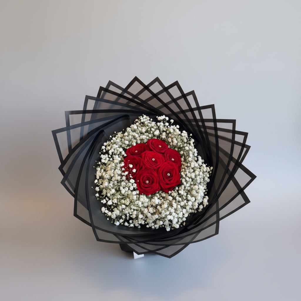 Bouquet of red roses and white baby's breath on a decorative black and white card.